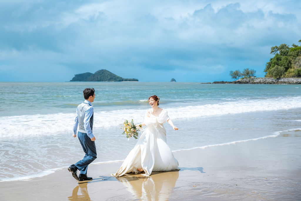 遠くに島が見える浜辺を手をつないで走る新郎新婦