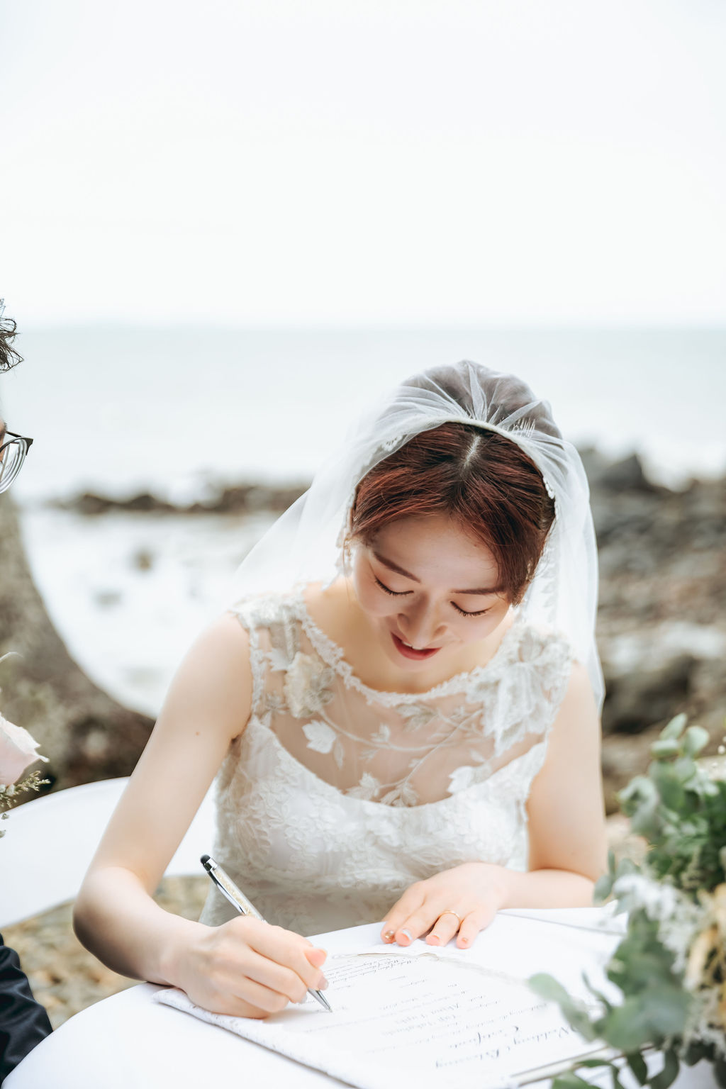 海を背にしたテーブルで結婚証明書にサインする花嫁